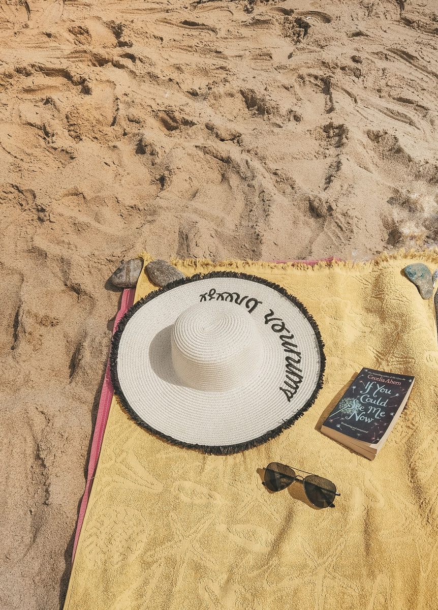 Sun hat, sunglasses and a book on a beach towel in bright sun