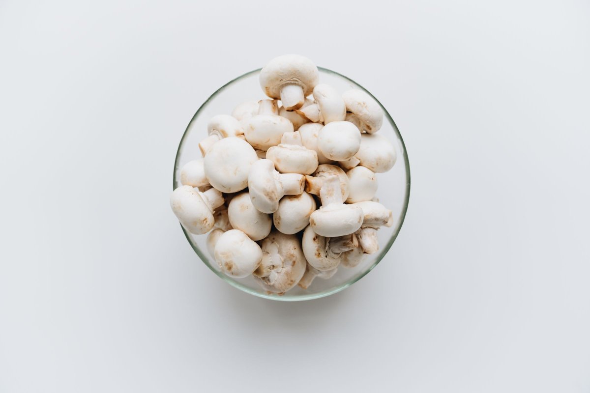 Fresh white mushrooms in a clear glass bowl on a white background