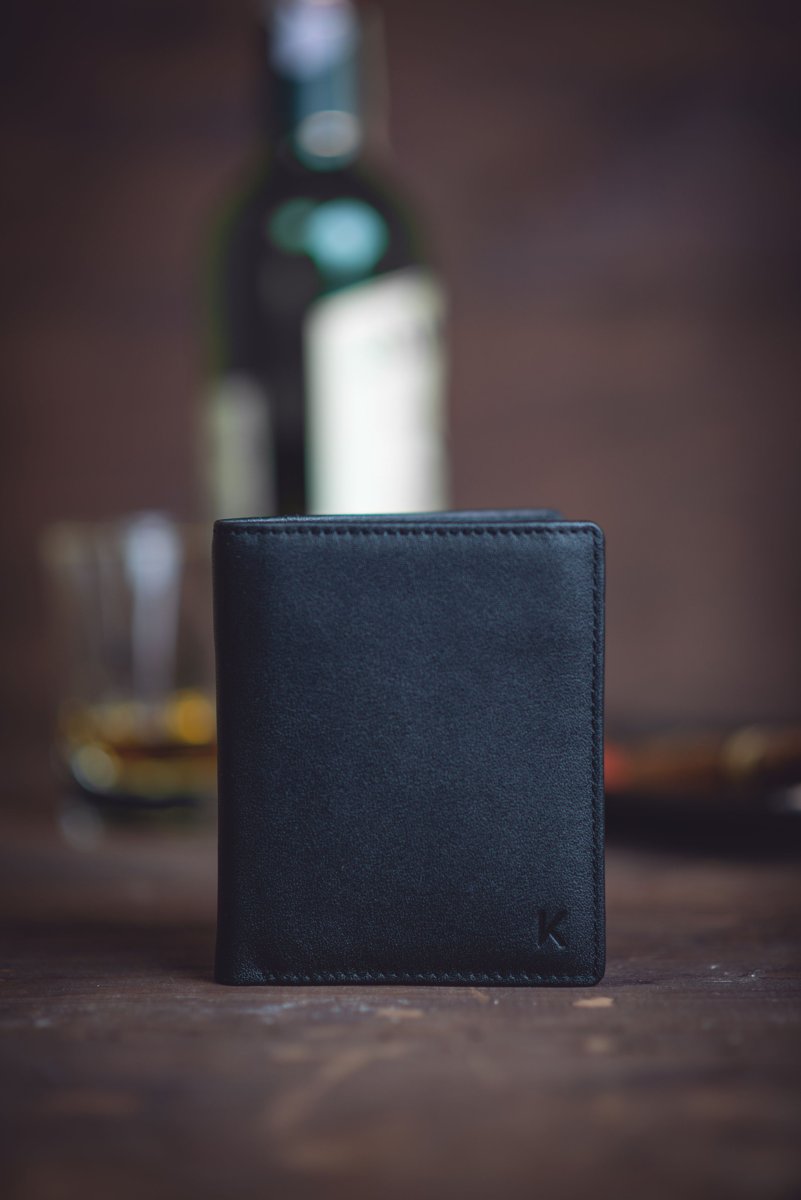Slim black leather wallet standing upright on a dark wooden table
